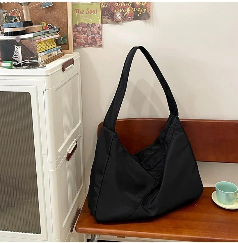 Oversized black nylon city sling bag displayed on a wooden bench in a minimalist everyday lifestyle scene