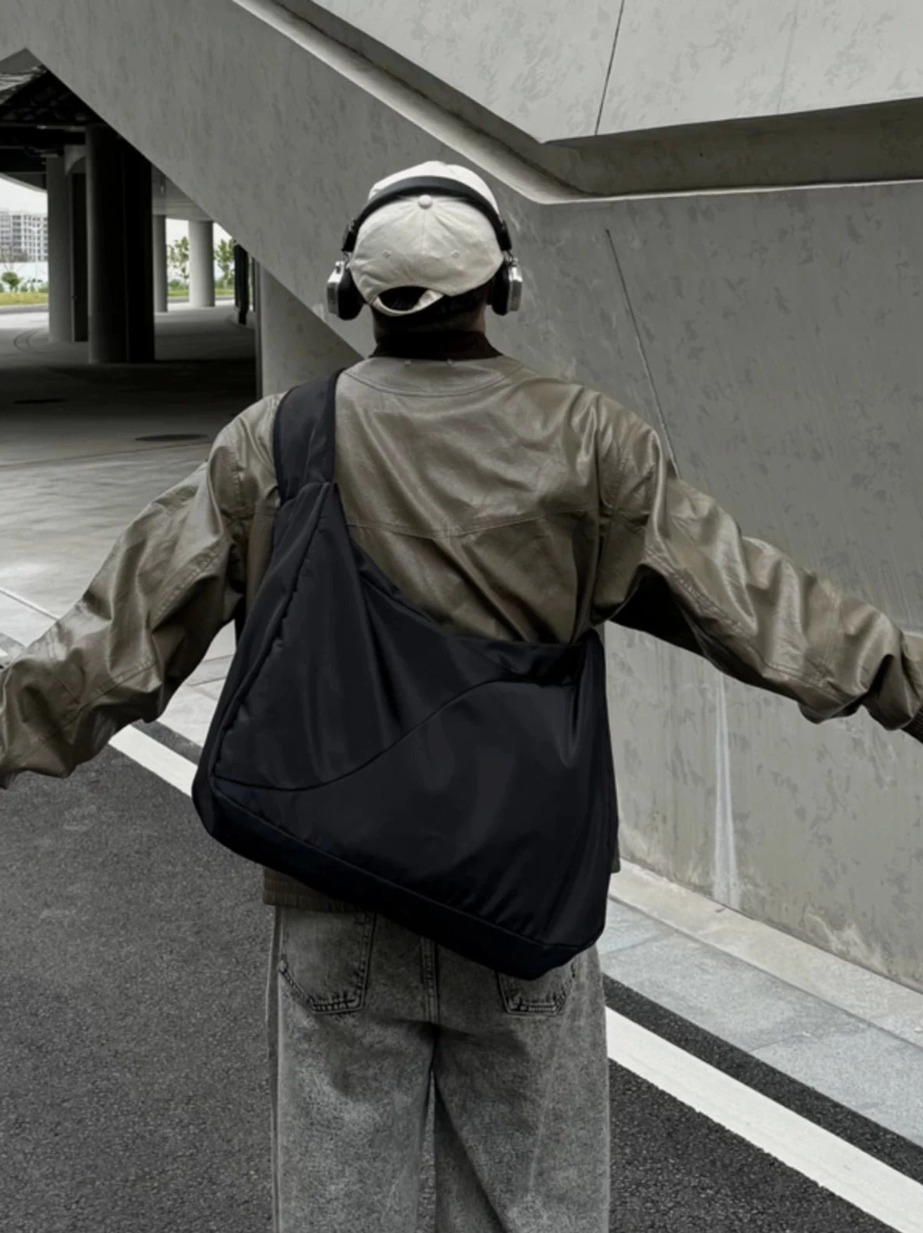 Large black nylon crossbody sling bag worn on the back in a relaxed urban Korean streetwear outfit