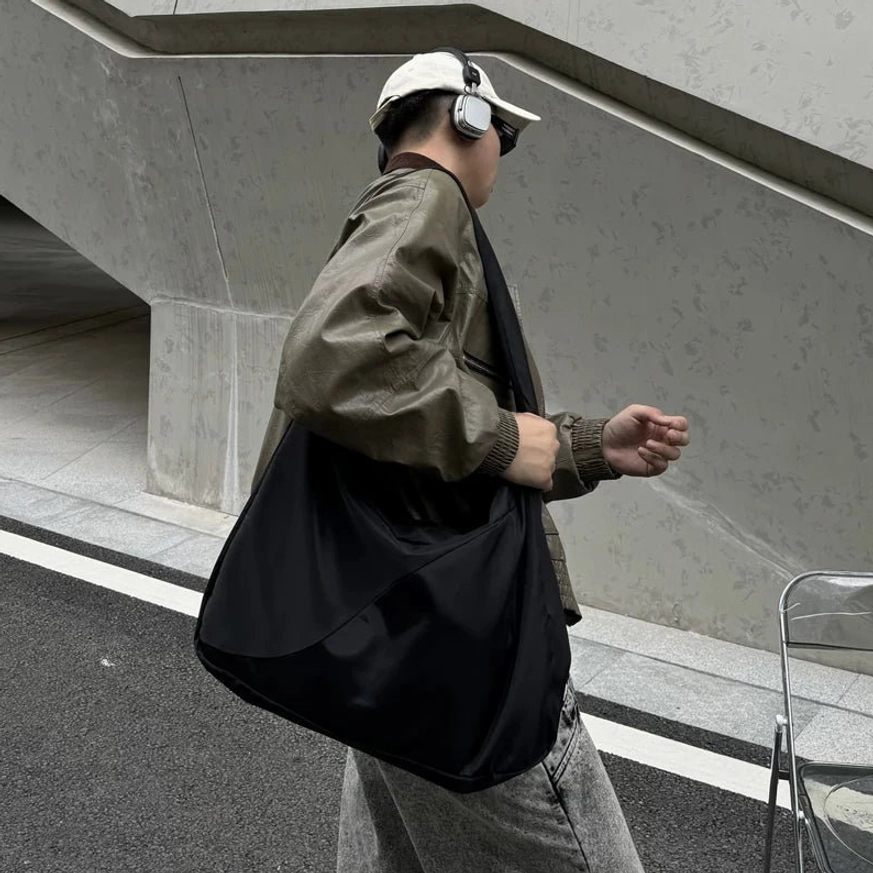 Oversized black nylon city sling bag with wide shoulder strap and large laptop-ready hobo interior