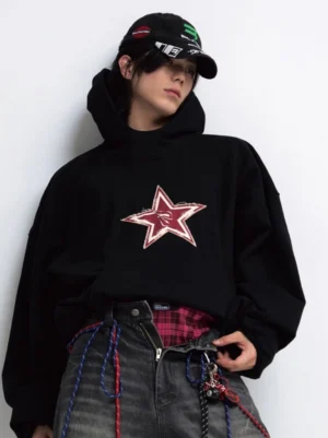 Male model wearing oversized black red star graphic hoodie with distressed chest print and baggy jeans front close-up