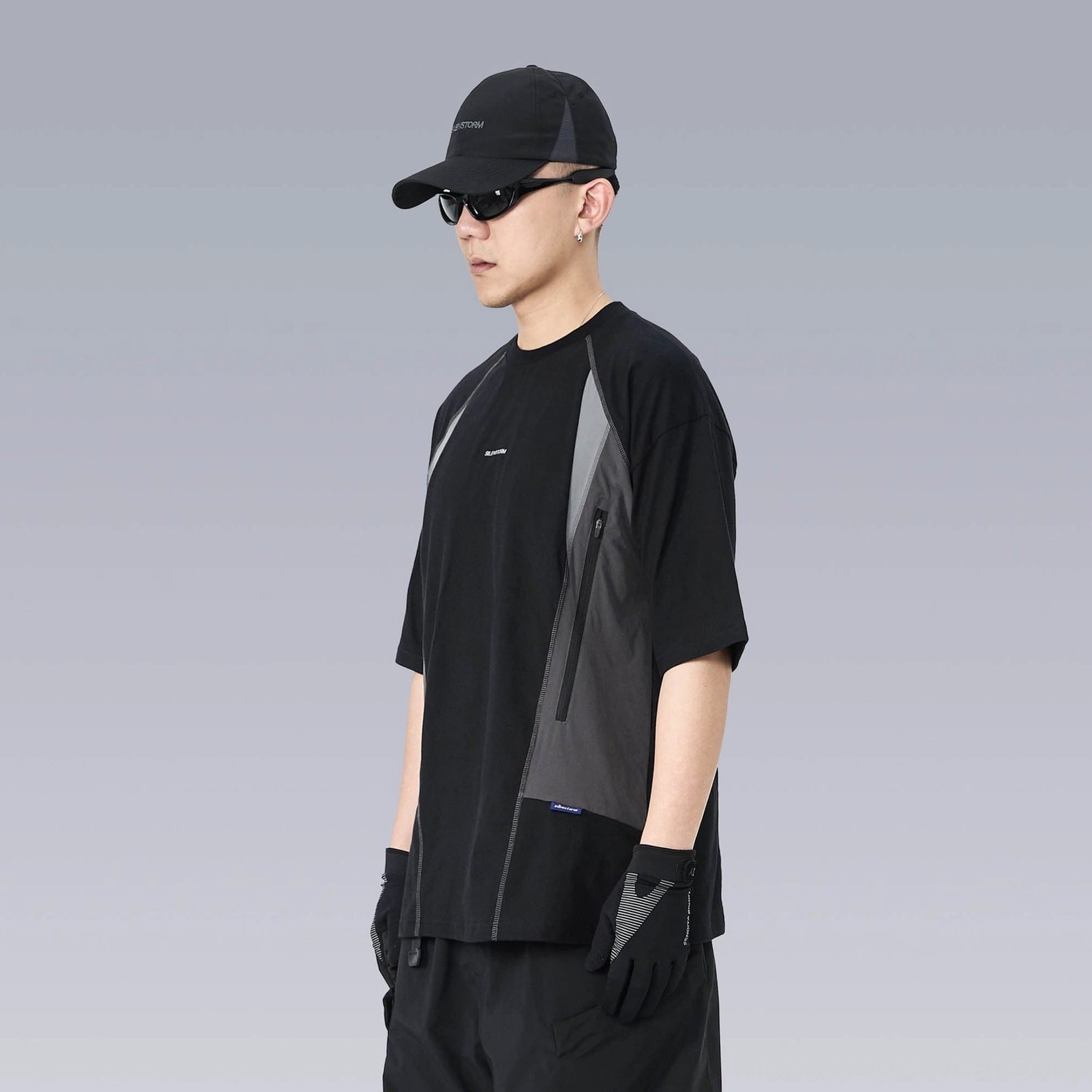 Right side view of an oversized black tech T-shirt with curved grey color blocking and a vertical zippered utility pocket