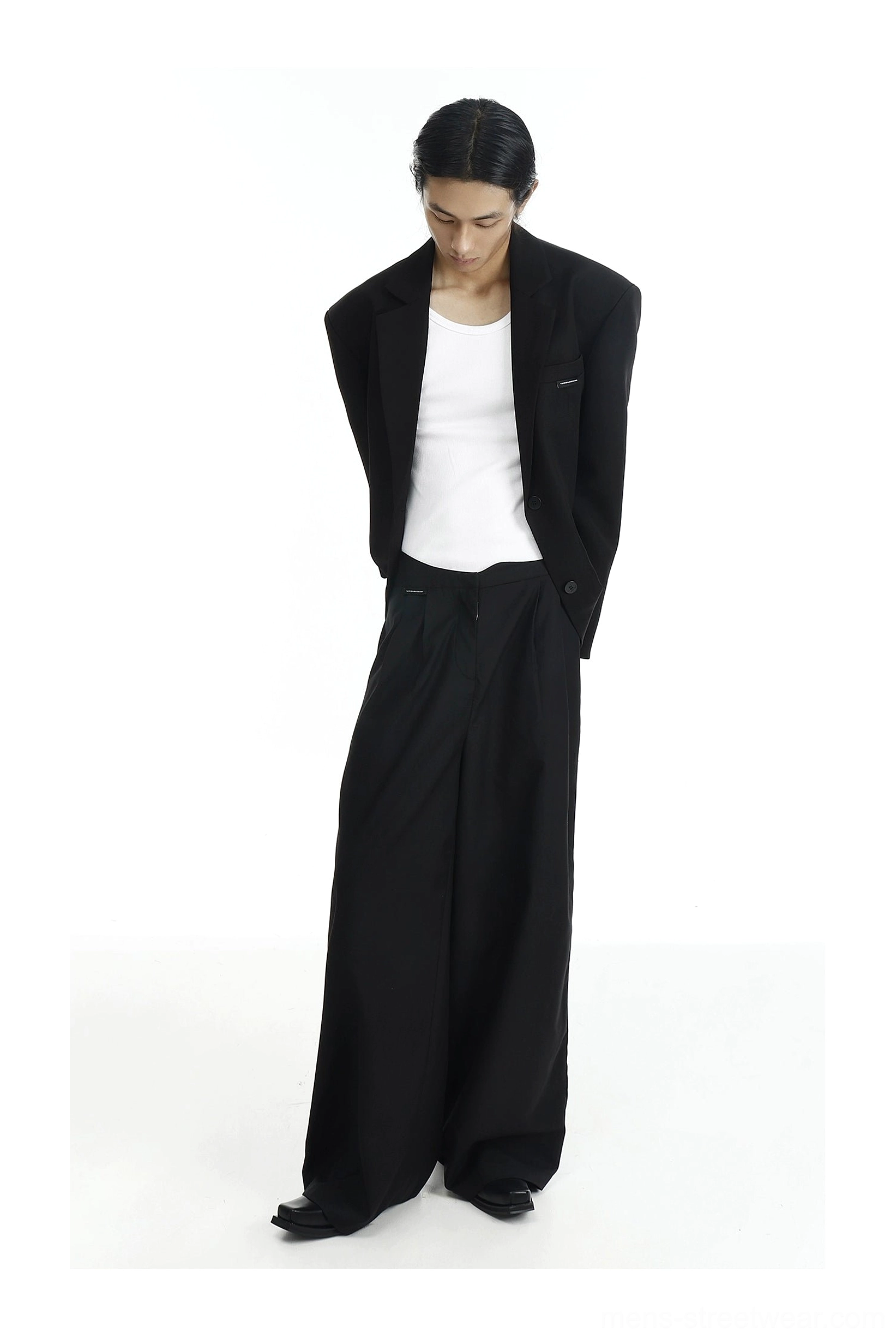 Oversized black two-button blazer front detail with notched lapel, flap pockets, subtle chest logo, and white T-shirt