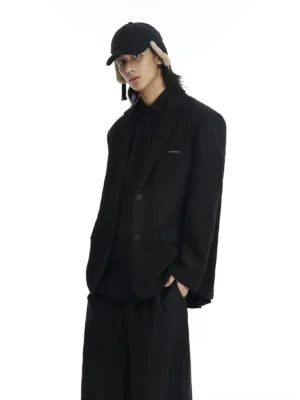 Oversized black two-button blazer in minimalist Seoul streetwear styling, three-quarter front view with black earflap cap