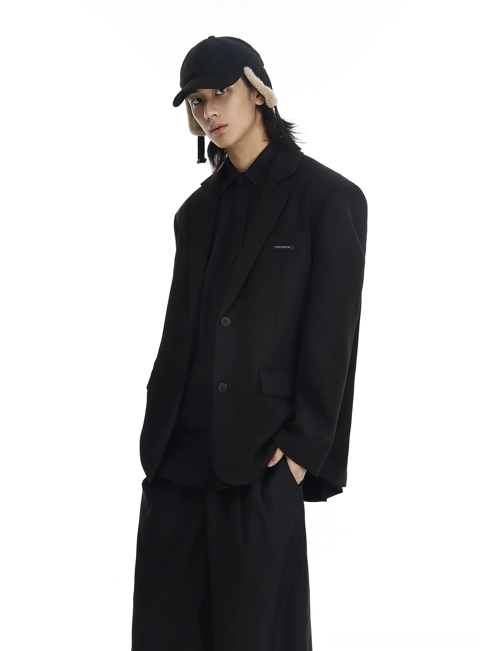 Oversized black two-button blazer in minimalist Seoul streetwear styling, three-quarter front view with black earflap cap