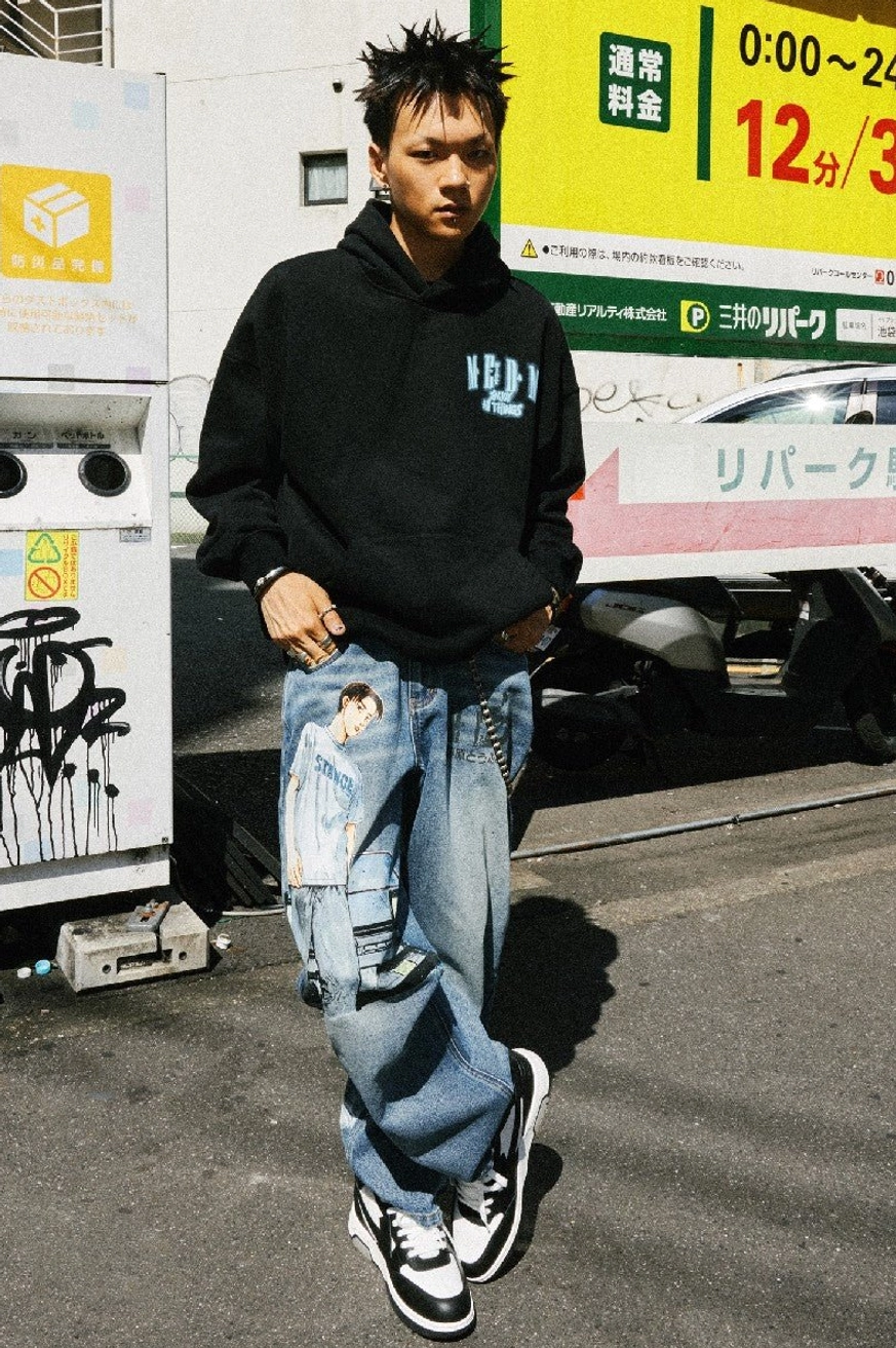 Black oversized hooded sweatshirt with light blue chest graphic styled with ripped jeans and skate shoes in a Japanese urban streetwear setting