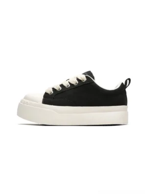 Black and white oversized cartoon platform sneakers shown from the side with canvas upper, rounded white toe cap, flat laces, and chunky rubber sole