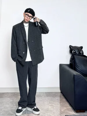 Front full-body view of an oversized black and white pinstripe double-breasted blazer and straight-leg pants suit set styled with a beret and square glasses