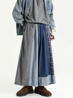 Oversized blue grey patchwork denim skirt pants in a low angle front view with wide legs, striped panels, plaid accents, and washed denim texture