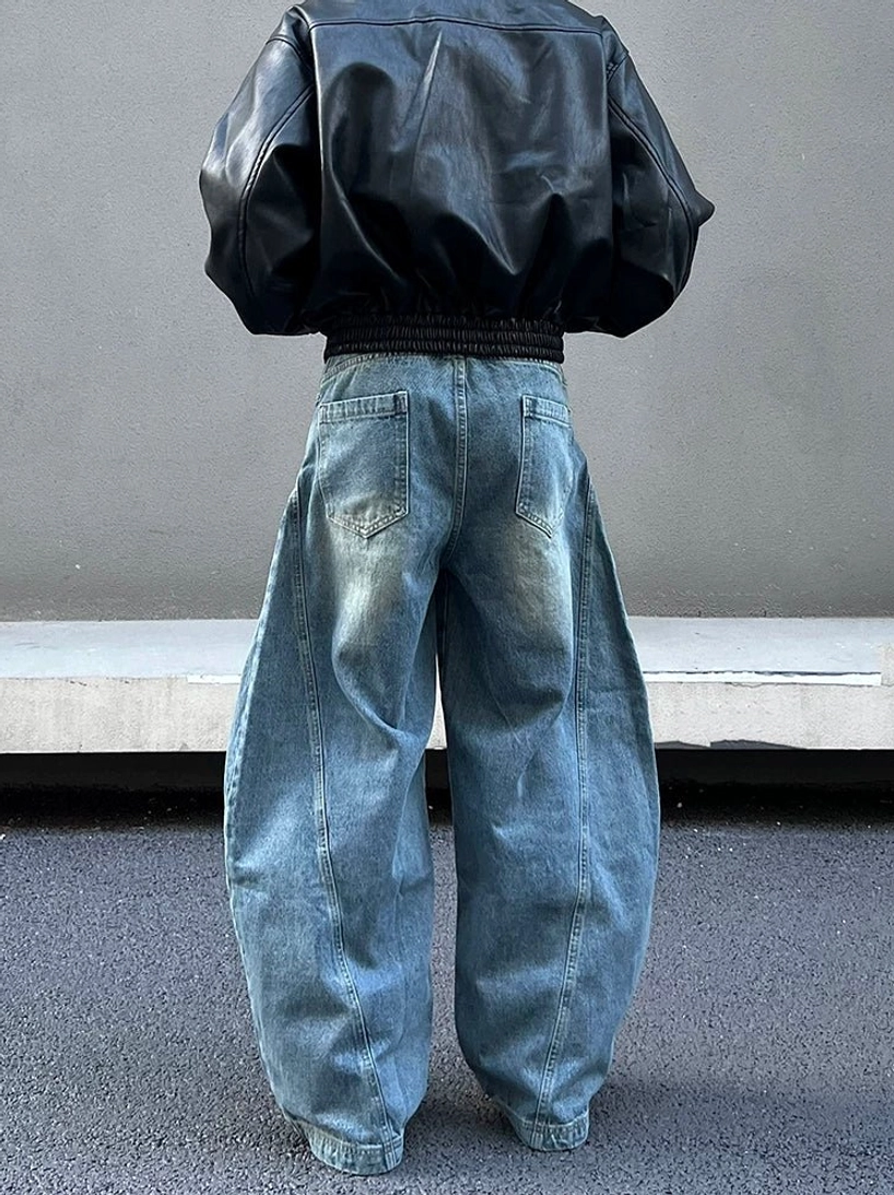 Back view of oversized vintage blue orbital panel jeans showing classic denim back pockets, wide-leg balloon silhouette, soft stacked hem, and cropped black leather jacket