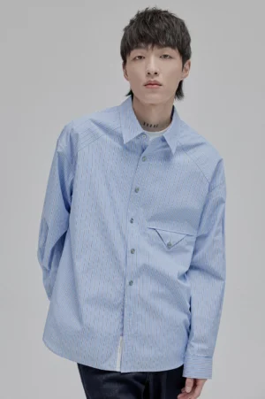Front view of an oversized light blue vertically striped shirt with angular flap chest pocket and relaxed streetwear fit