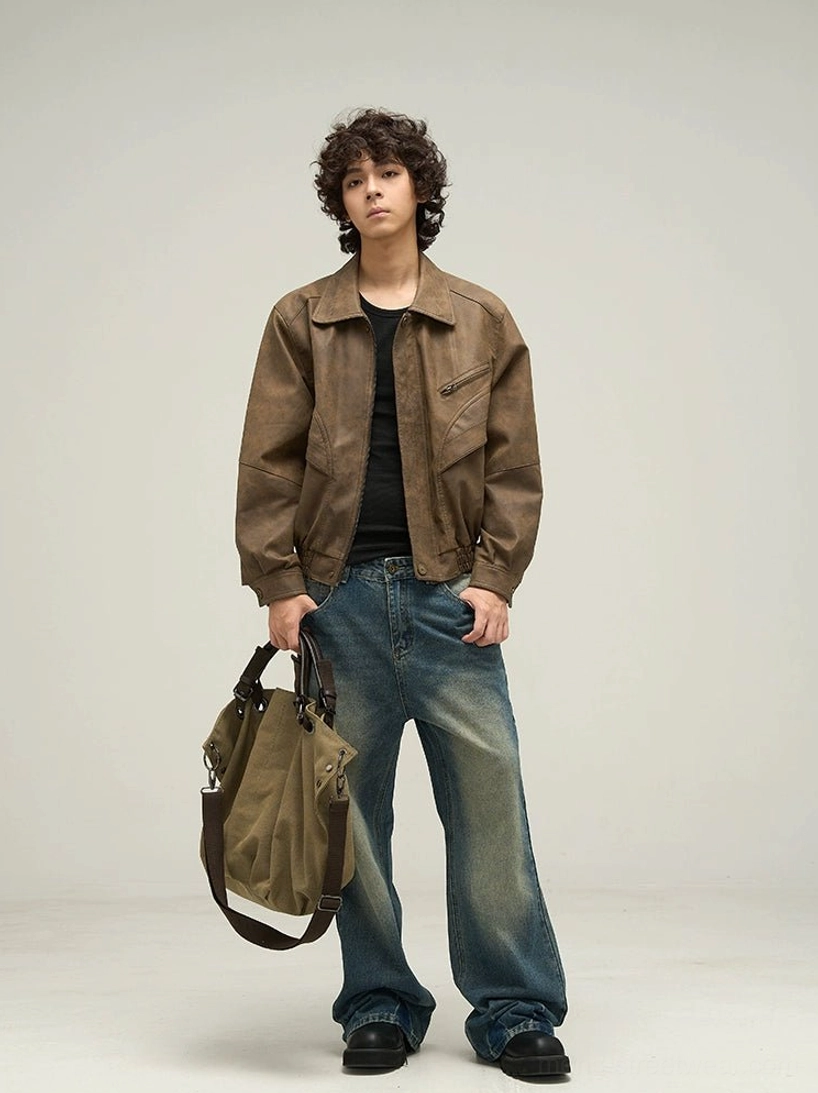 Full-body view of a man wearing an oversized brown faux leather jacket with wide-leg blue jeans, black shoes, and a khaki shoulder bag