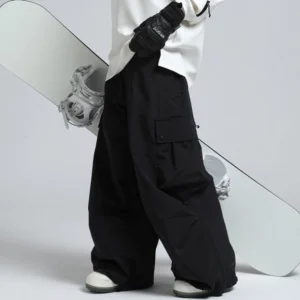 Black oversized cargo snow pants with wide legs and flap pockets styled beside a snowboard