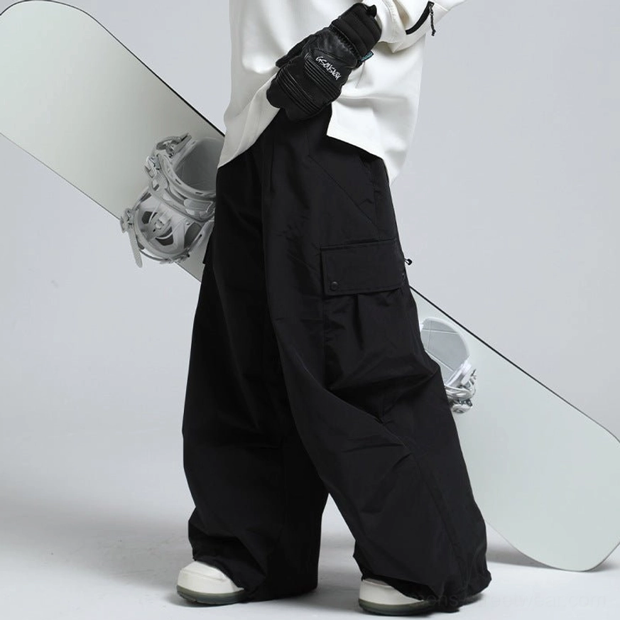 Black oversized cargo snow pants with wide legs and flap pockets styled beside a snowboard