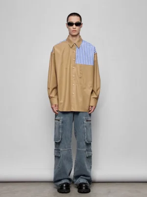 Front full-body view of an oversized khaki color-block patchwork shirt with blue and white striped shoulder panels styled with cargo denim jeans
