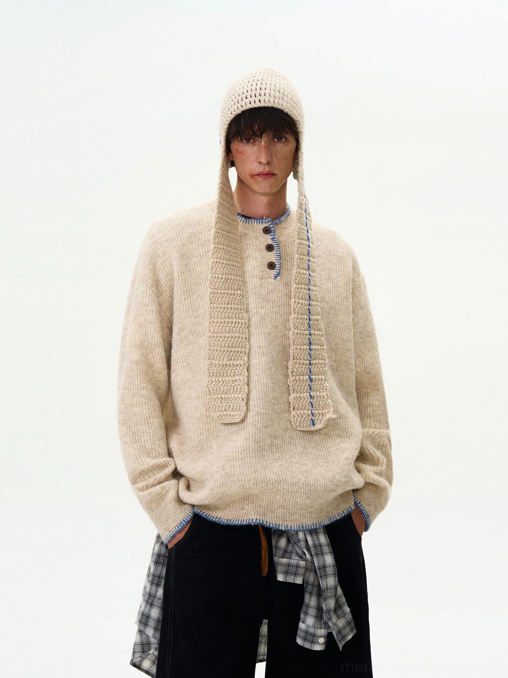 Apricot oversized contrast-stitch Henley knit sweater shown on a male model with a relaxed Korean streetwear silhouette, layered plaid shirt detail, and matching knitted headwear