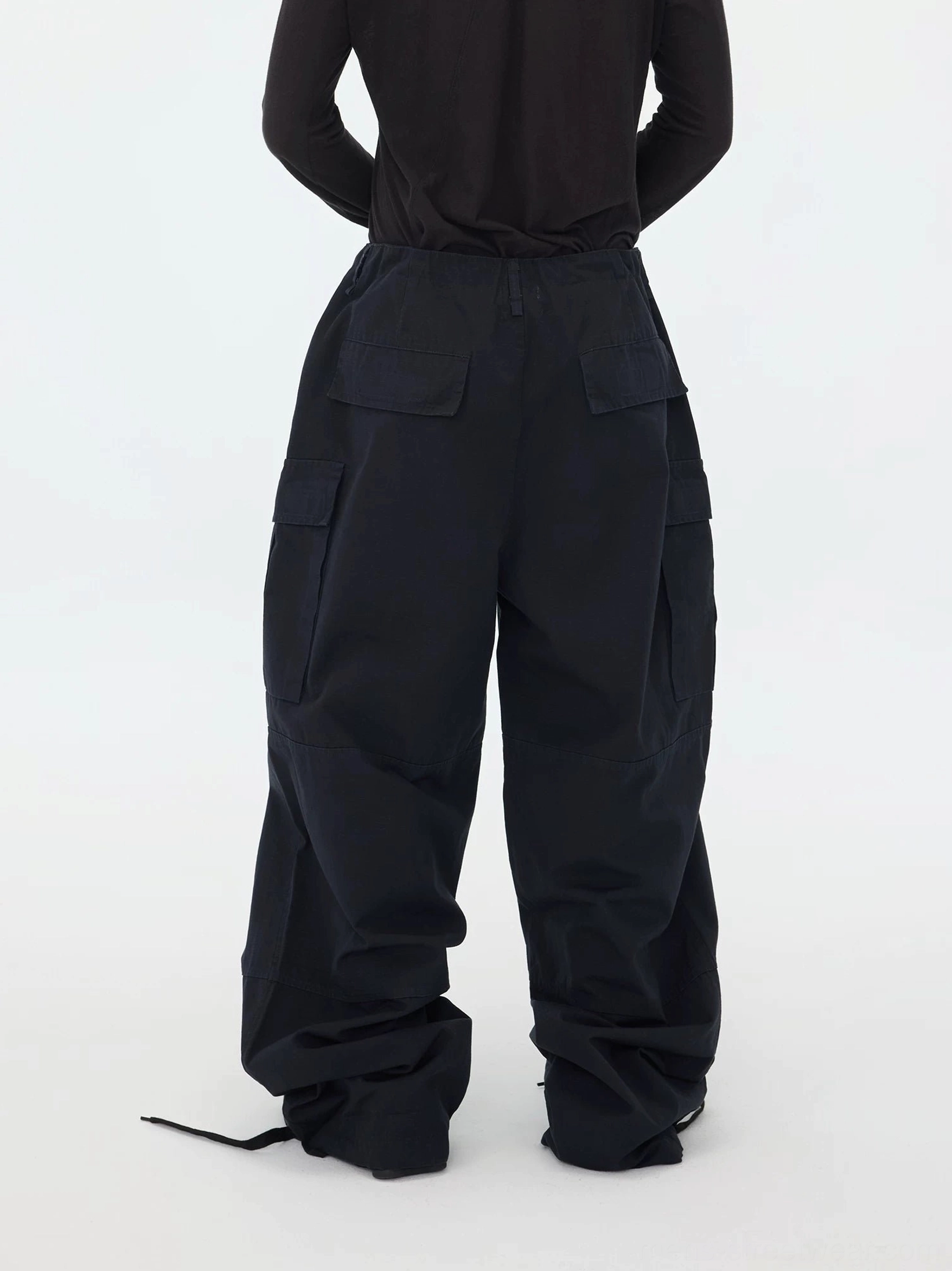Rear full-body view of oversized dark blue cargo trousers without footwear, showing rear patch pockets, wide legs, and adjustable stacked ankle hems