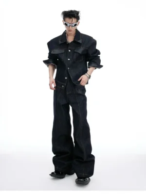 Full-body front view of a male model wearing an oversized dark indigo denim jacket with matching wide-leg jeans, silver sunglasses, and contrast topstitching in a white studio
