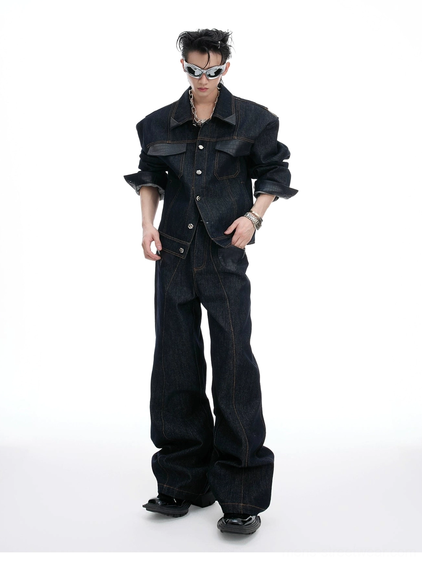 Full-body front view of a male model wearing an oversized dark indigo denim jacket with matching wide-leg jeans, silver sunglasses, and contrast topstitching in a white studio