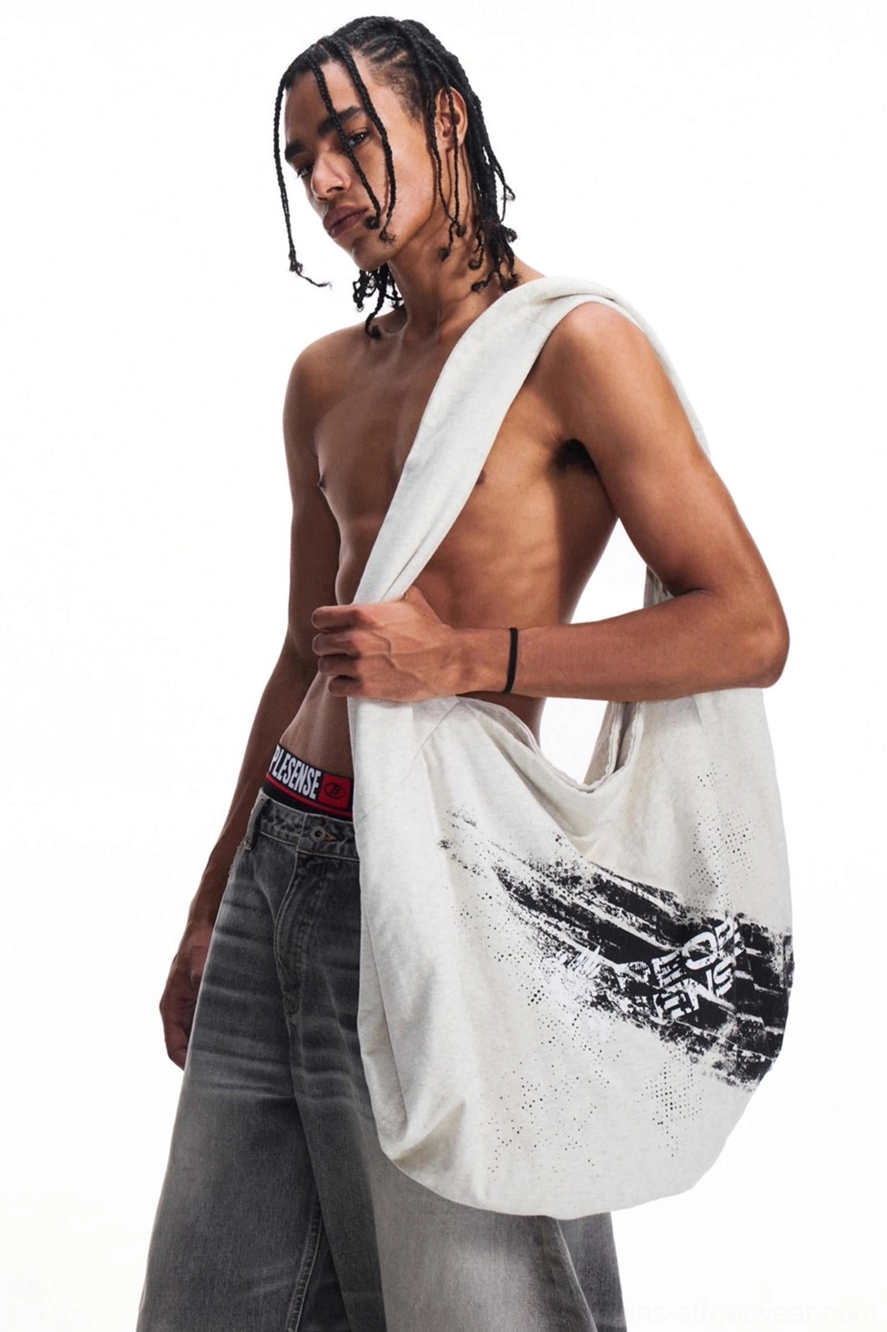 Side view of an oversized distressed canvas shoulder tote bag with faded black graphic print styled with baggy gray denim