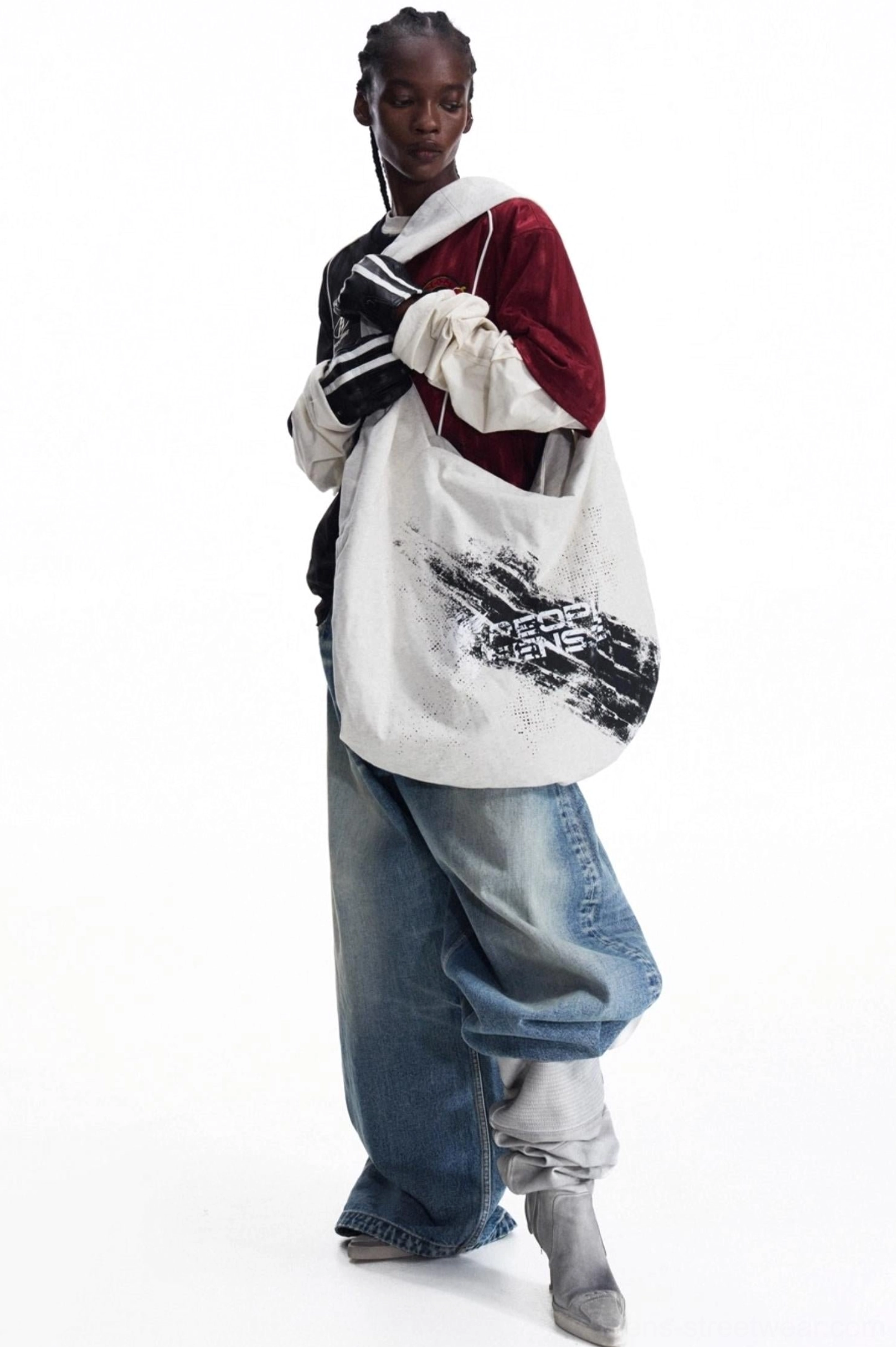 Front three-quarter view of an oversized distressed canvas tote bag with black brushstroke print and wide-leg blue jeans