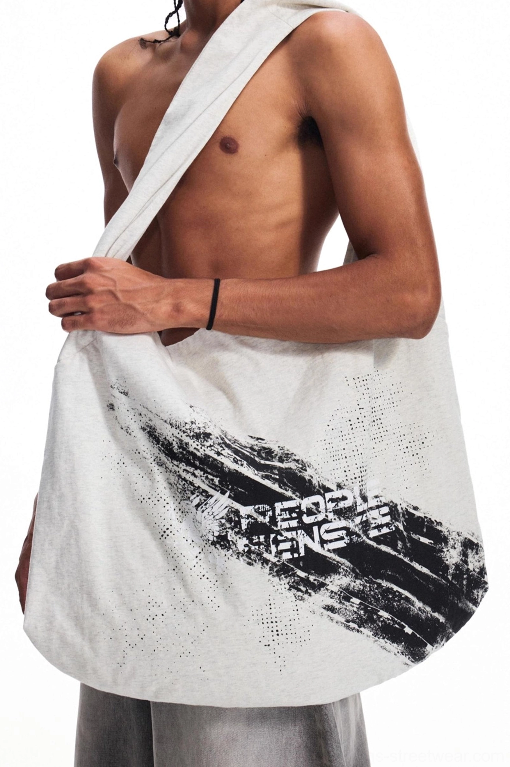 Oversized distressed gray canvas tote bag with black brushstroke graphic print worn over one shoulder in a men's streetwear outfit