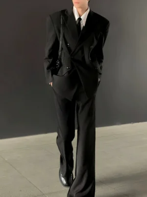 Front three quarter view of an oversized double breasted black suit set with structured shoulders wide leg trousers white shirt black tie and crossbody bag