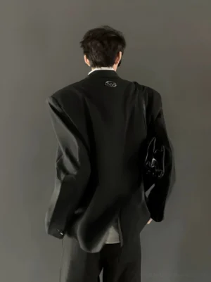 Rear view of an oversized double breasted black blazer and wide leg suit trousers with subtle back logo detail and leather shoulder bag