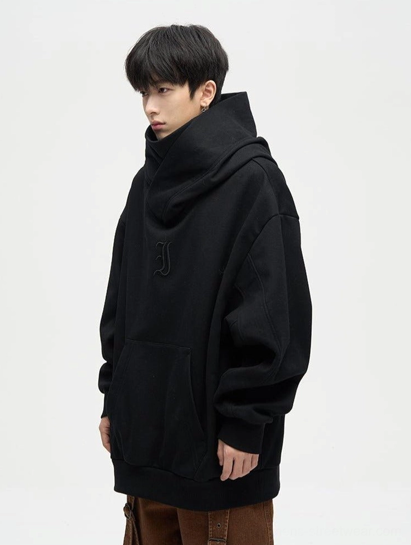 Black oversized dual-layer high-neck hoodie front view with wrap neck hood kangaroo pocket and tonal embroidered chest motif