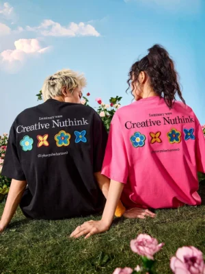 Oversized floral patch graphic T-shirt shown from the rear three-quarter view with colorful flower appliques and Creative Nuthink slogan in a sunny flower field