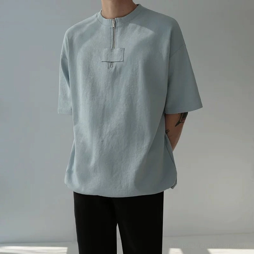 Hazy blue oversized half-zip cotton tee on male model with dropped shoulders and utility chest panel