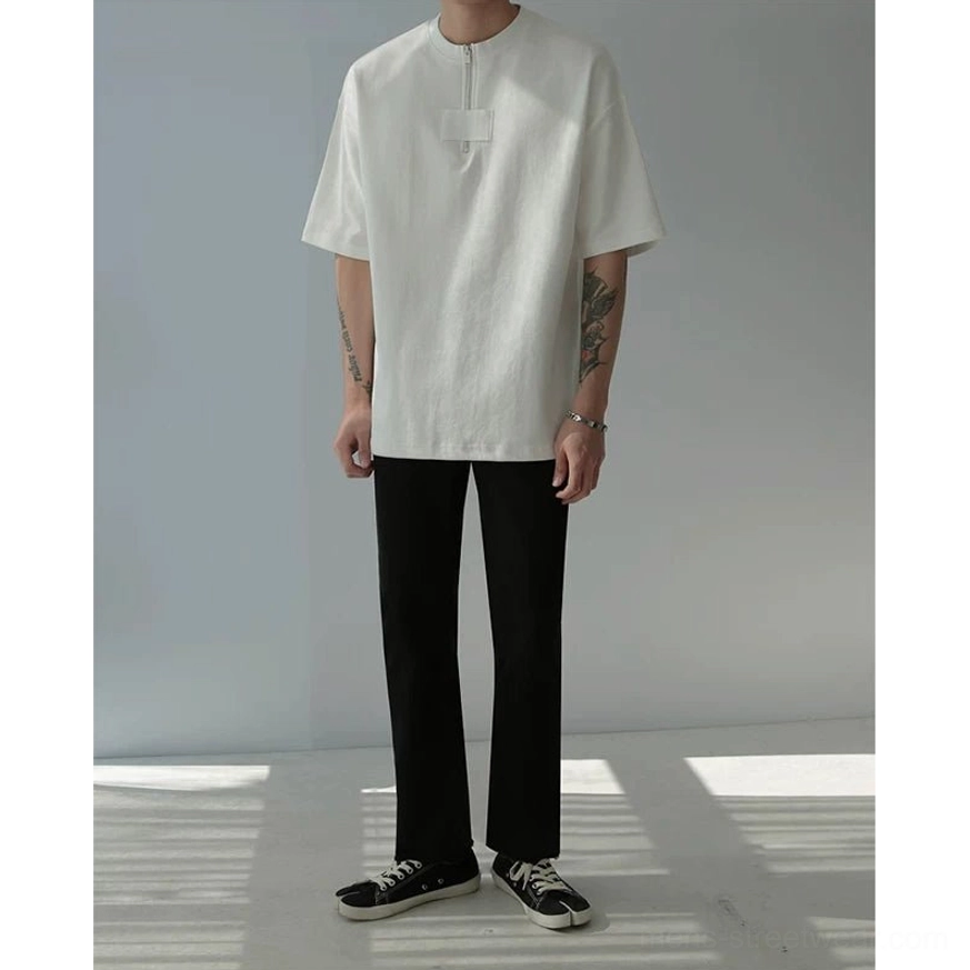 Male model styling a light oversized half-zip cotton tee with black trousers and low top sneakers