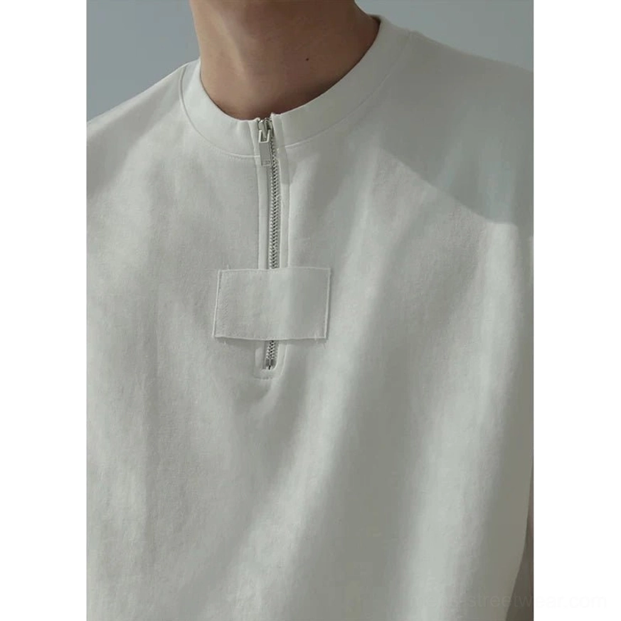 Close-up front view of oversized half-zip cotton tee with rectangular utility chest panel and metal zipper detail