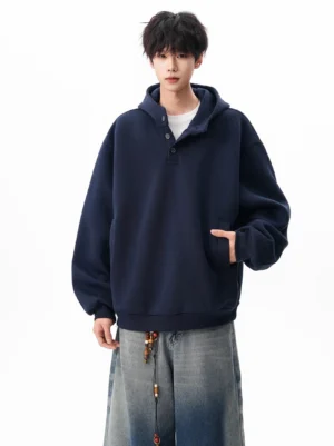 Navy blue oversized Henley hooded sweatshirt shown from the front with a four-button placket, drop shoulders, side pockets, and wide-leg jeans