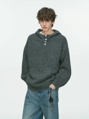 Charcoal gray oversized hooded Henley knit sweater with fuzzy texture, drop shoulders, button placket, and kangaroo pocket styled with blue denim jeans