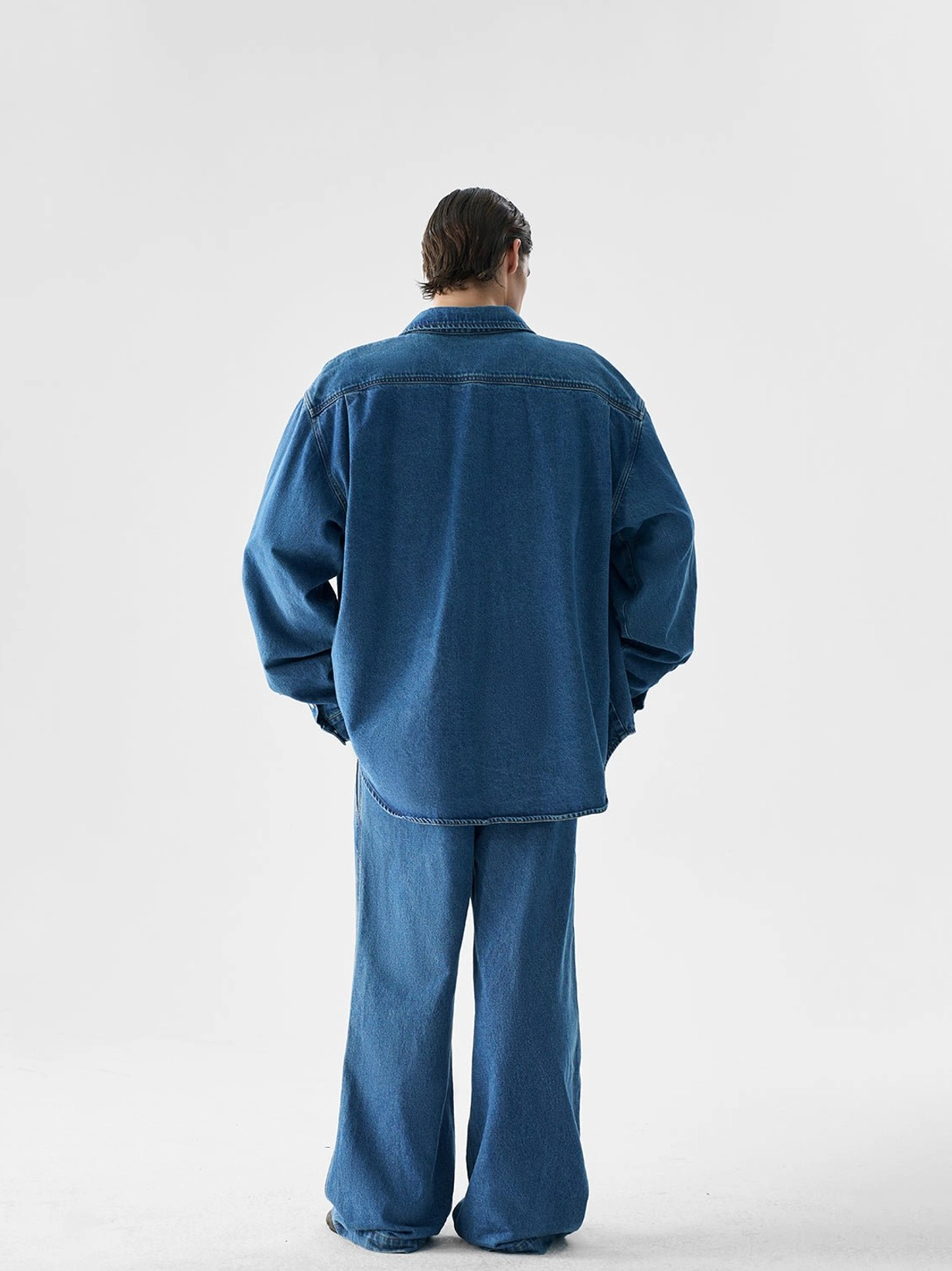 Back view of an oversized indigo denim shirt jacket and wide-leg pants set showing the back yoke seam and relaxed fit