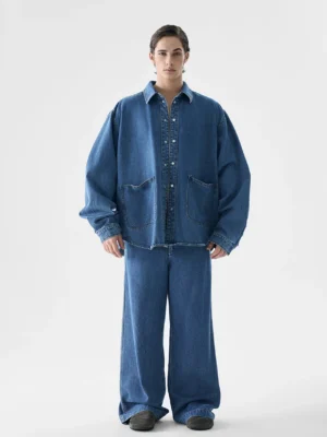 Front view of an oversized indigo denim jacket and wide-leg pants streetwear set worn by a male model in a white studio