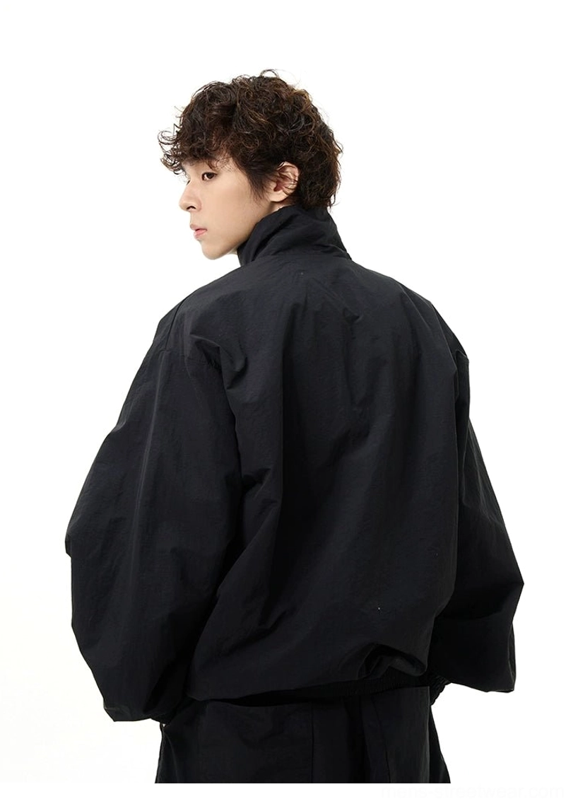Back three-quarter view of an oversized matte black windbreaker with dropped shoulders and clean logo-free design