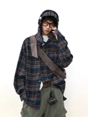Male model wearing an oversized navy red plaid hooded shirt with olive cargo pants headphones and crossbody bag in a three-quarter studio view