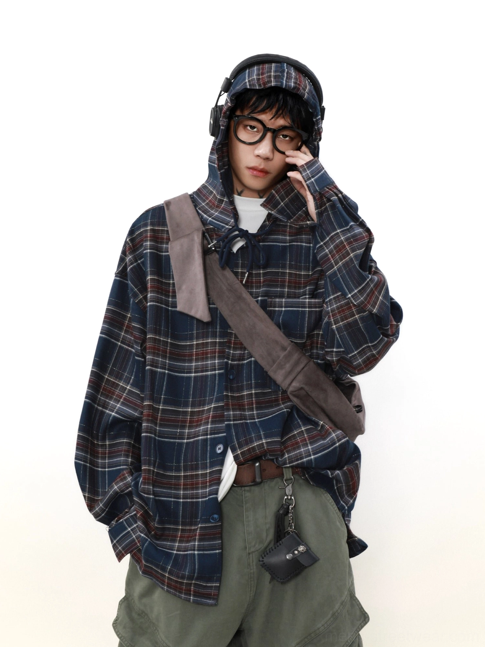 Male model wearing an oversized navy red plaid hooded shirt with olive cargo pants headphones and crossbody bag in a three-quarter studio view