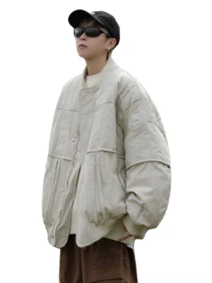 Front view of an oversized off-white quilted bomber jacket with ribbed stand collar, dropped shoulders, textured padded fabric, and large utility patch pockets