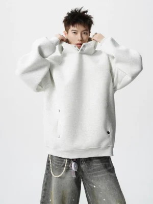 Oversized off white snap neck fleece hoodie styled with splatter wide leg jeans and waist chain in a minimalist studio