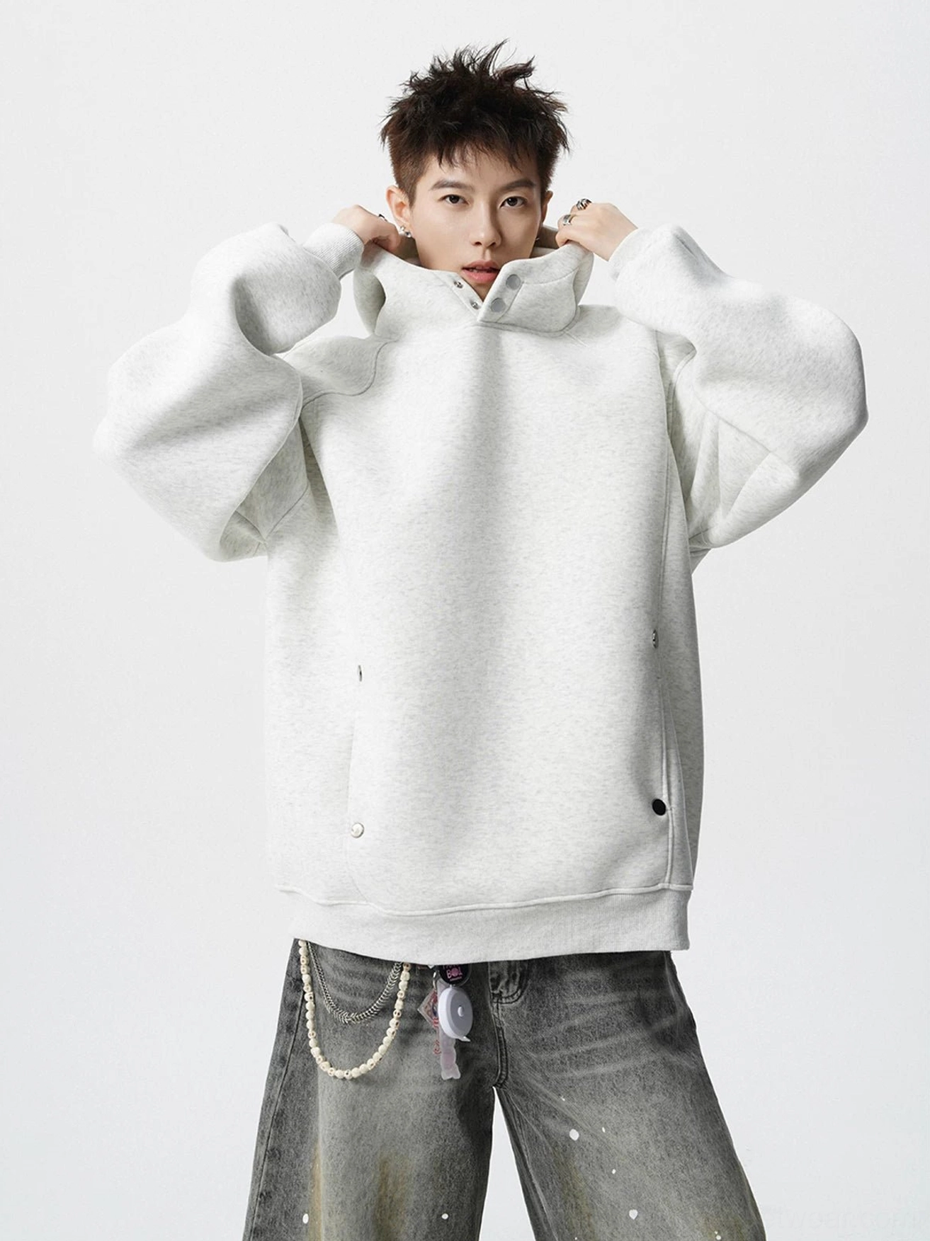 Oversized off white snap neck fleece hoodie styled with splatter wide leg jeans and waist chain in a minimalist studio