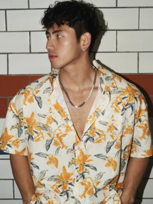 Close-up side view of an oversized orange and cream tropical floral camp shirt with short sleeves, notch collar, and grey leaf print