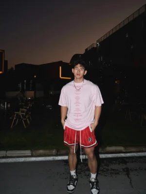 Back view of oversized pink graphic streetwear t-shirt worn with red striped basketball shorts sport sneakers and white socks outdoors at night