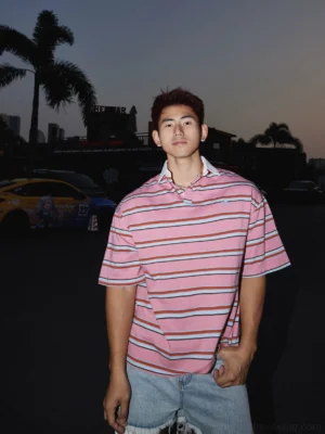Front full-body view of oversized pink striped rugby polo shirt with contrast white collar in a dusk parking lot