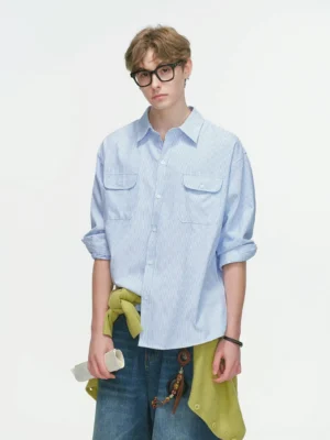 Light blue oversized utility work shirt shown from the front with button closure, dual chest pockets, rolled sleeves, and wide-leg denim styling