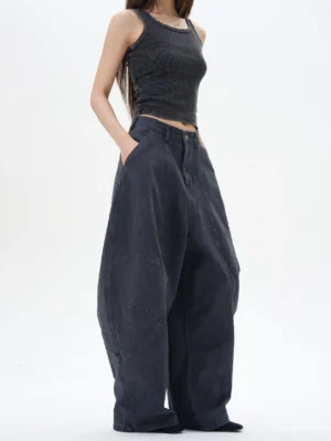 Female model wearing oversized dark washed pleated wide leg denim pants with curved panel seams and a high rise in a minimalist studio