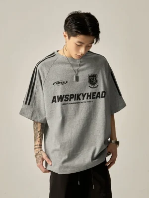 Oversized heather grey raglan athletic graphic tee front three-quarter view with black stripe sleeve trims and chest brand emblems, styled with black loose trousers