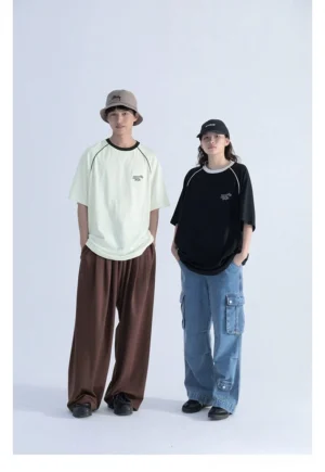 Front full-body view of oversized raglan sleeve graphic T-shirt in black and off-white with contrast crew neck, shoulder piping, and subtle chest embroidery