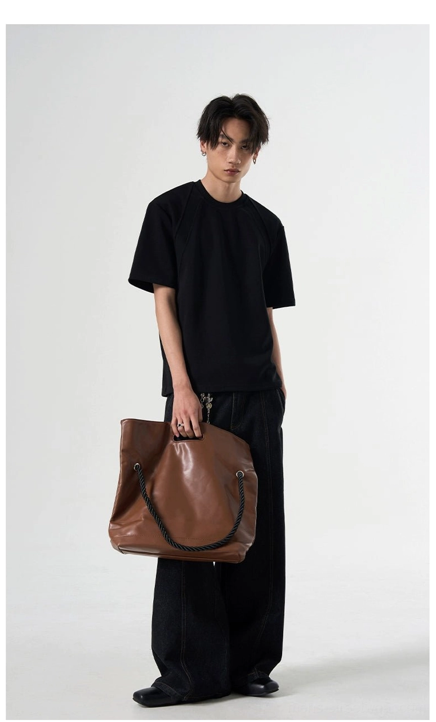 Black oversized raglan T-shirt shown in a full-body front view with a relaxed silhouette and brown leather tote bag